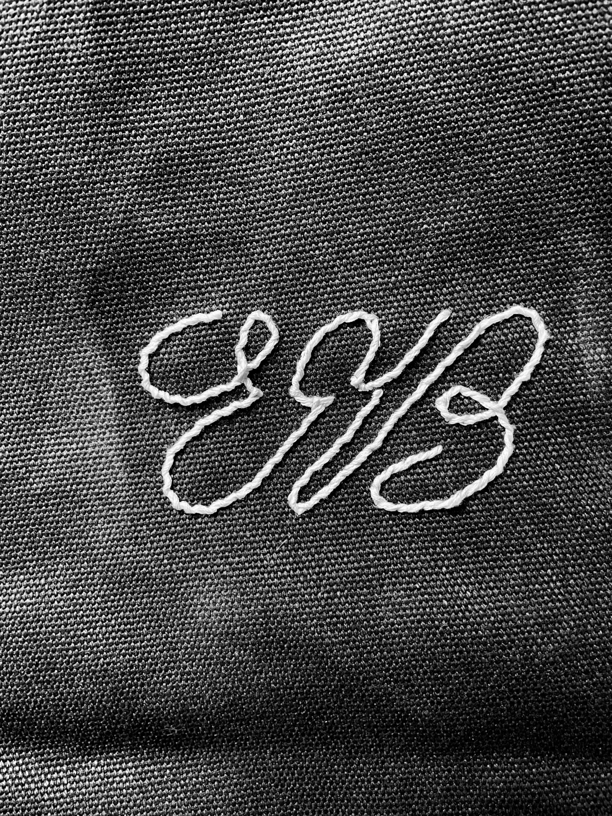 Monogramme brodé au fil blanc sur une toile de lin